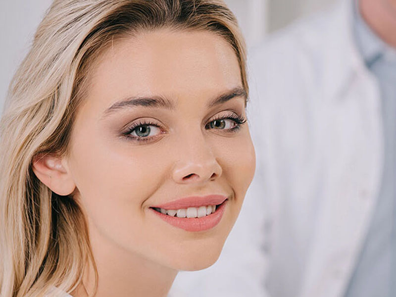 Smiling patient in a dental clinic with a professional in the background, representing trusted and recommended dental care in Fairfax, VA