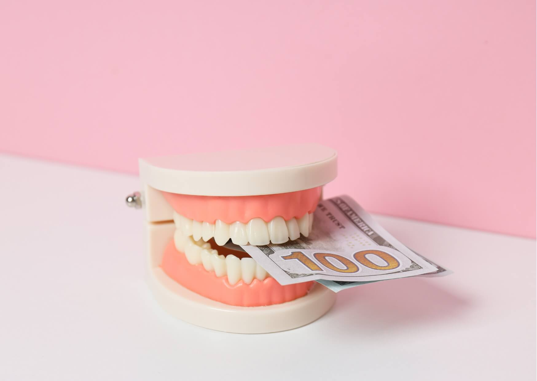 Dental model holding a $100 bill, illustrating the factors that influence the cost of dental implants.